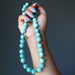 Hand holding an Amazonite beaded necklace against a dark background