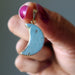 Hand holding a blue Amazonite crescent moon pendant with gold outline