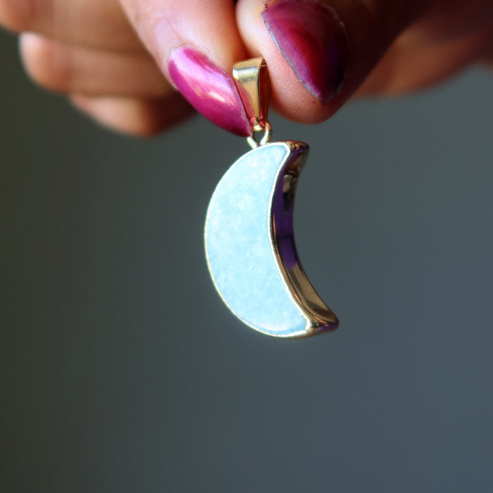 Amazonite Crescent moon-shaped pendant held by a hand with pink nail polish against a gray background