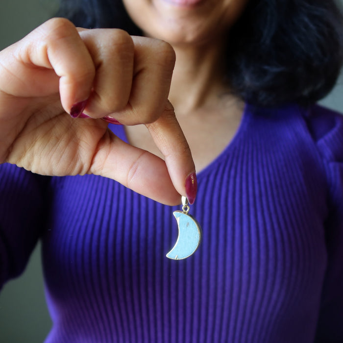 Person holding an Amazonite crescent moon-shaped pendant with a gold chain.