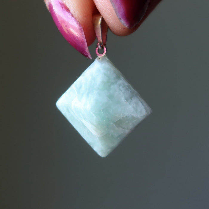 Amazonite pyramid pendant held by a hand with pink nail polish against a dark background