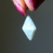 Light blue Amazonite pyramid pendant held by a hand with pink nail polish against a dark background