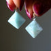 Amazonite pyramid pendants held between fingers against a neutral background