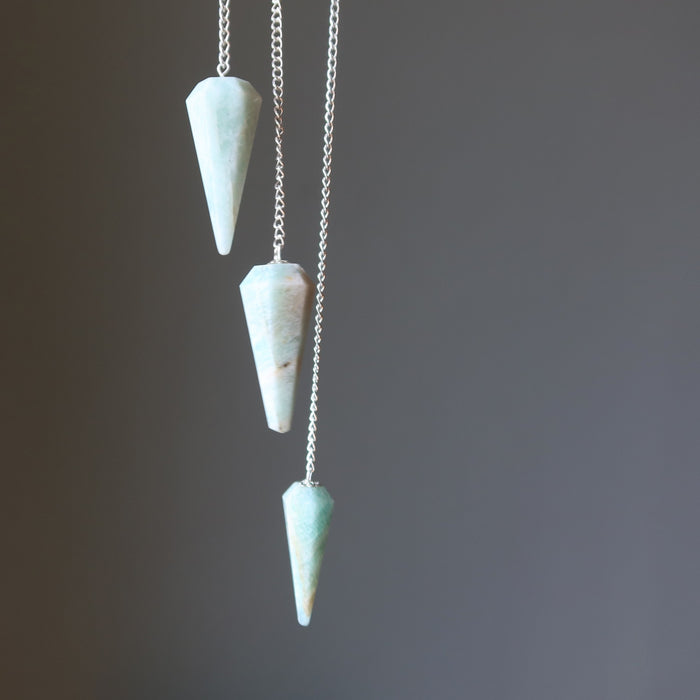 Three amazonite pendulums on silver chains against a dark background