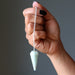 Hand holding a light blue amazonite crystal pendulum against a dark background