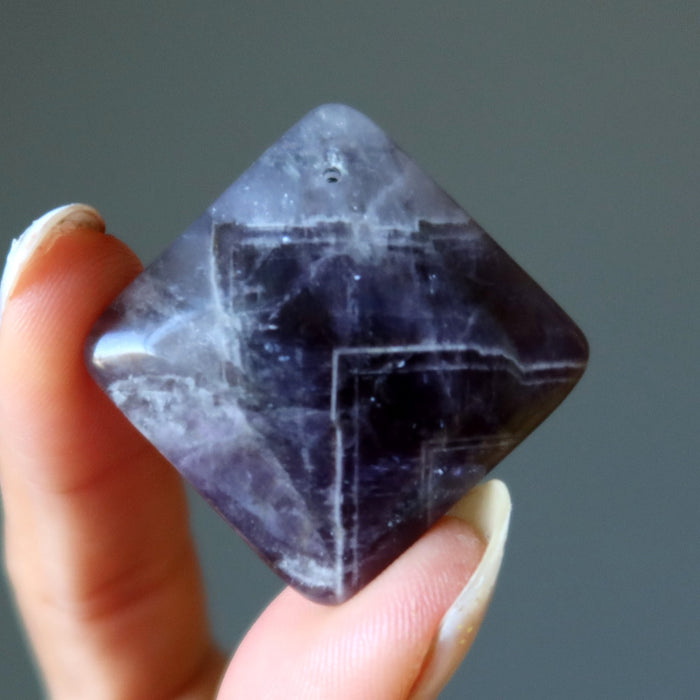 Person holding a faceted purple Amethyst crystal against a gray background