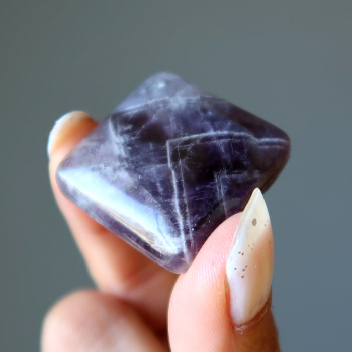 Hand holding a purple Amethyst crystal against a gray background