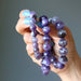 Hand holding a stack of purple chevron amethyst beaded bracelets against a gray background