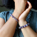 Close-up of hands wearing chevron amethyst purple beaded bracelets with a blurred background
