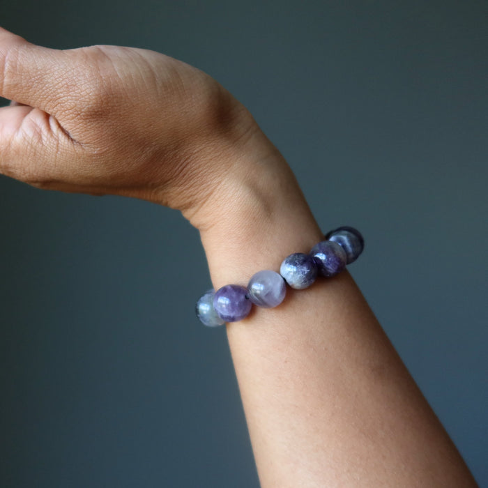 Hand wearing a bracelet with chevron amethyst purple and white beads against a dark background