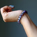 Hand wearing a purple chevron amethyst beaded bracelet on a dark background