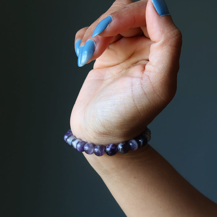 Hand wearing a purple chevron amethyst beaded bracelet against a dark background