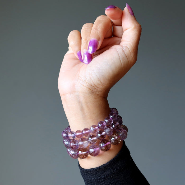 Hand wearing a stack of purple beaded amethyst bracelets on a gray background