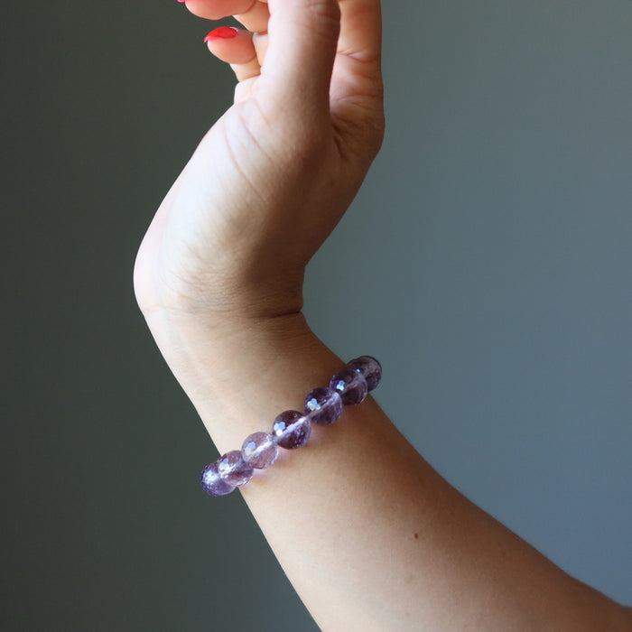 Hand wearing a purple faceted amethyst beaded bracelet against a gradient background