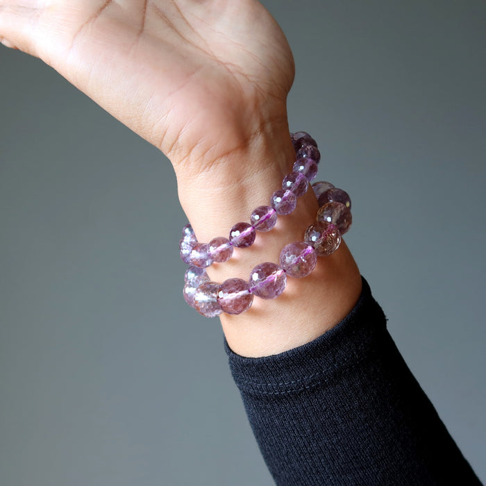 Purple amethyst beaded bracelet on a wrist against a gray background