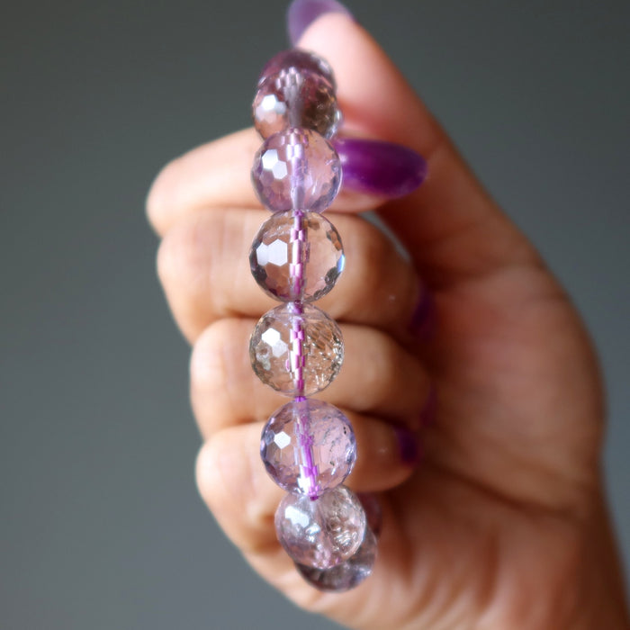 Hand holding an amethyst necklace with purple and clear beads against a neutral background