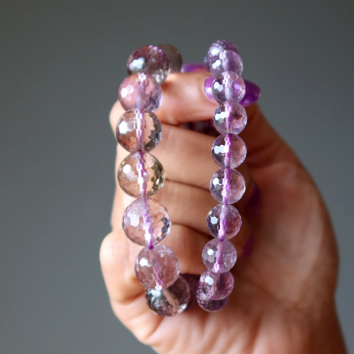 Hand holding two purple amethyst beaded bracelets against a gray background