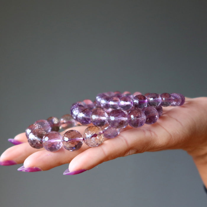 Hand holding a bracelet with purple amethyst beads against a gray background