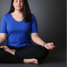 Person in a blue shirt and black pants sitting in a meditative pose on a dark background