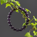 Purple amethyst beaded bracelet on a branch with green leaves against a dark background