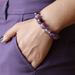 Close-up of a hand wearing a purple amethyst beaded bracelet on a matching purple background