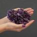 Hand holding a large purple amethyst crystal against a dark background