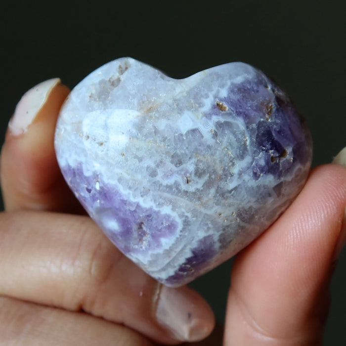 Heart-shaped purple and white amethyst stone held in a hand against a dark background