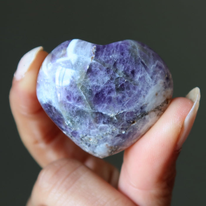 Hand holding a purple amethyst crystal against a dark background