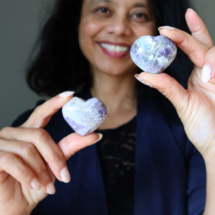 Woman holding two heart-shaped purple amethyst stones against a neutral background