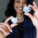 Woman holding two heart-shaped purple amethyst stones against a neutral background