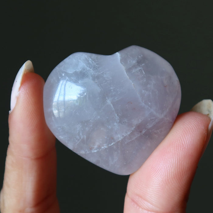 Heart-shaped amethyst crystal held between fingers against a dark background