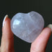 Heart-shaped amethyst crystal held between fingers against a dark background
