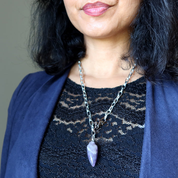 Person wearing a dark blue cardigan and black lace top with a silver necklace featuring a purple amethyst pendant.