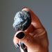 Hand holding a rough black apache tear obsidian stone against a neutral background