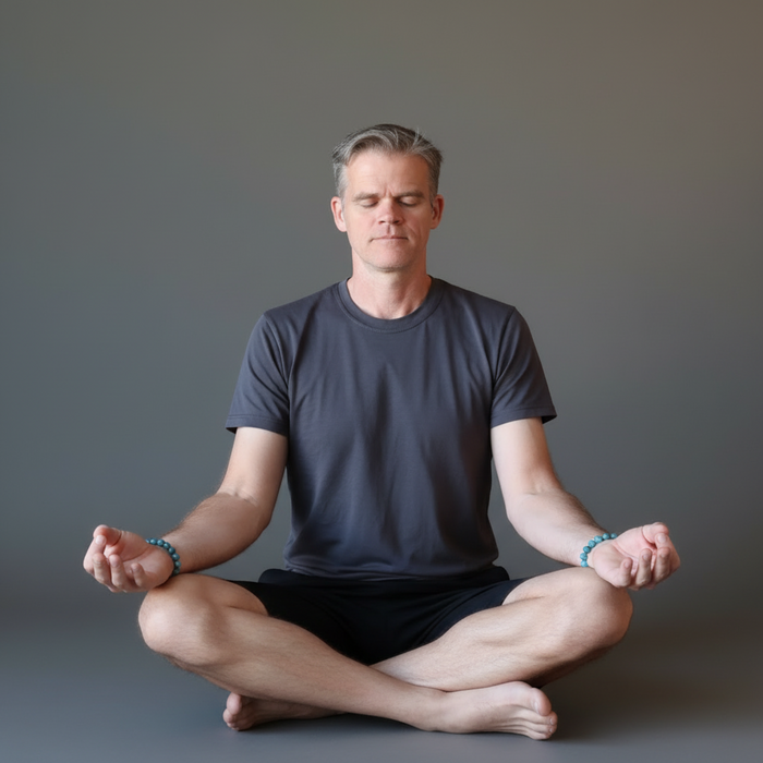 Man in a dark t-shirt and shorts sitting in a meditative pose with apatite bracelets