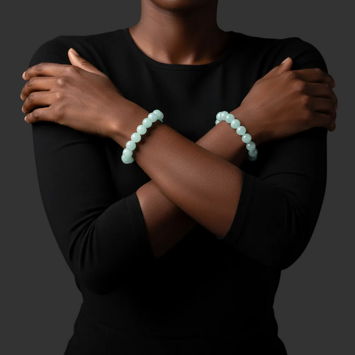 Person wearing two light aquamarine beaded bracelets on a dark background
