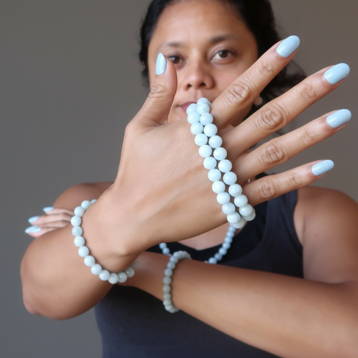Woman wearing multiple aquamarine beaded bracelets on a gray background