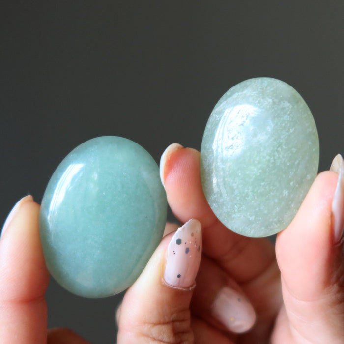 Two green aventurine oval cabochon stones held between fingers against a dark background
