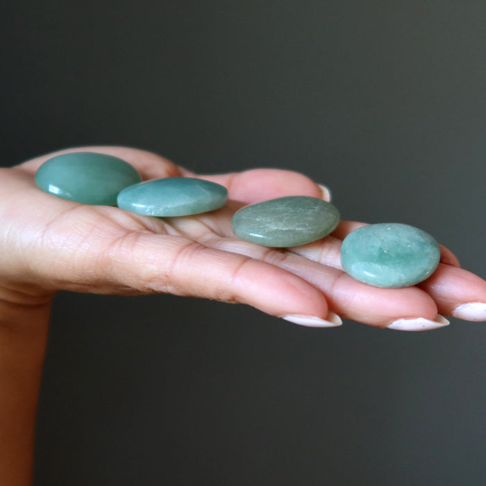 Hand holding four green green aventurine oval cabochon stones against a dark background