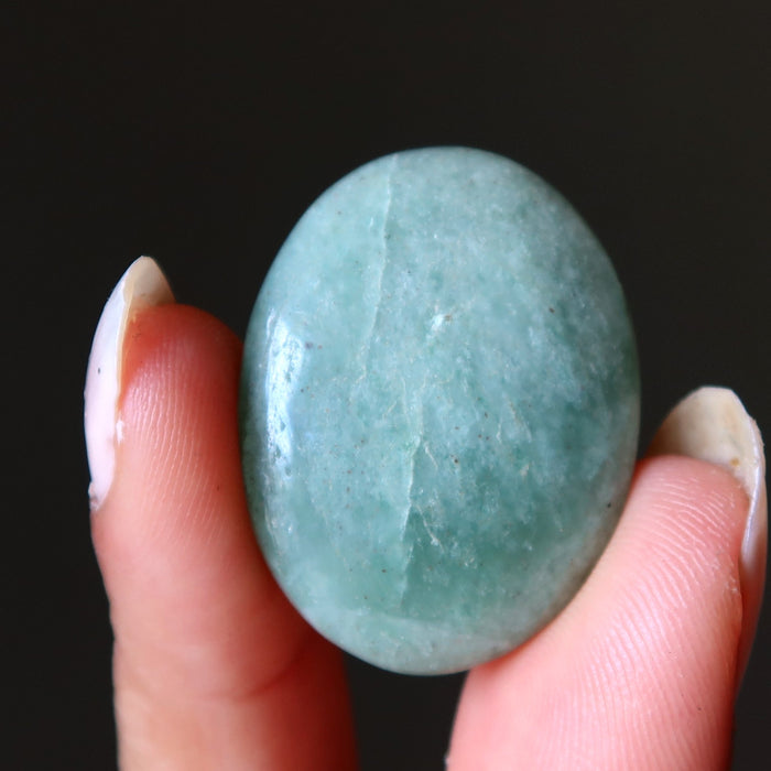 Hand holding a green green aventurine oval cabochon stone against a black background