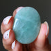 Hand holding a greenish-blue green aventurine oval cabochon stone against a dark background