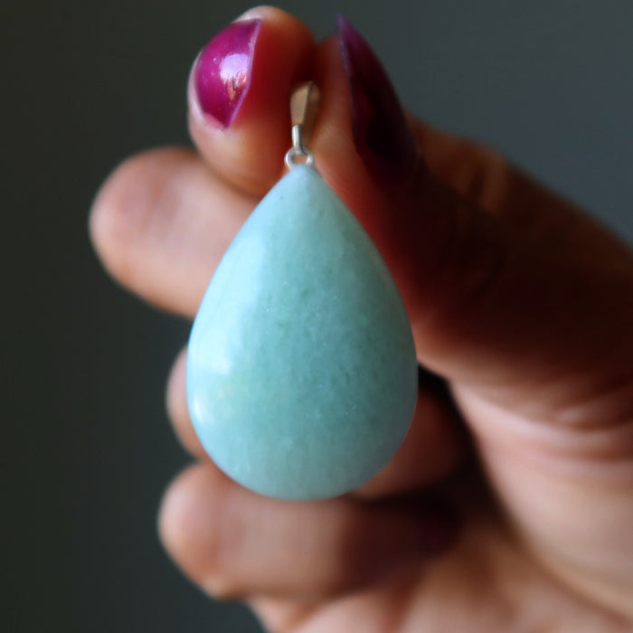 Aventurine teardrop-shaped earring held between fingers against a dark background