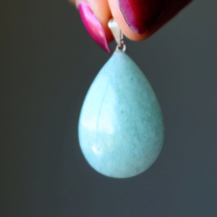 Teardrop-shaped Aventurine pendant held by a hand with pink nail polish against a dark background