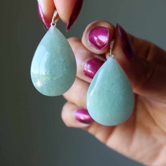 Aventurine Teardrop-shaped light blue earrings held by a hand with pink nail polish against a dark background