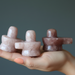 Three pink stone sculptures held in a hand against a gray background