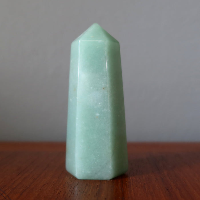 Green Aventurine crystal pyramid on a wooden surface with a neutral background