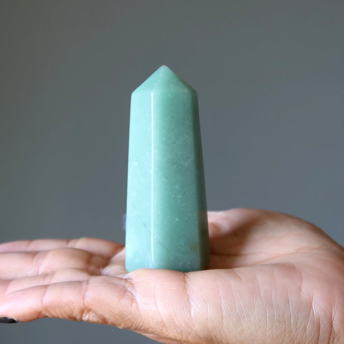 Hand holding a green Aventurine crystal against a gray background