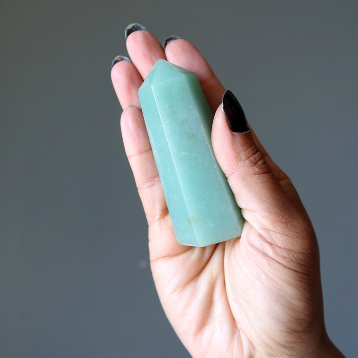 Hand holding a green Aventurine crystal against a gray background