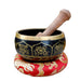 Decorative singing bowl with gold patterns on a red cushion, surrounded by yellow flowers and wooden elements.