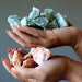 Hands holding green and orange raw calcite crystals against a gray background